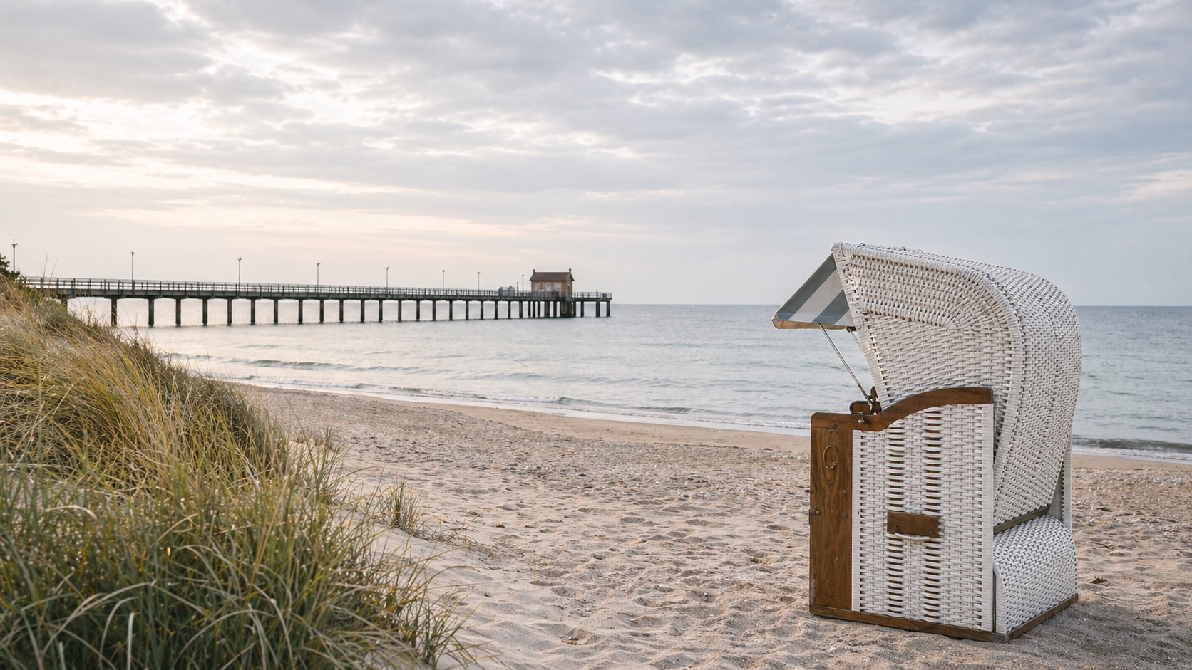 Weißer Strandkorb am Ostseestrand mit Seebrücke im Hintergrund; Favorent verwaltet Ferienimmobilien an der Küste.