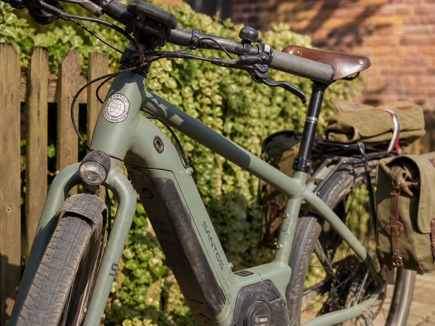 Graues E-Bike der Marke Santos mit Packtaschen vor Holzzaun, passend für Radtouren ab Ferienunterkunft.
