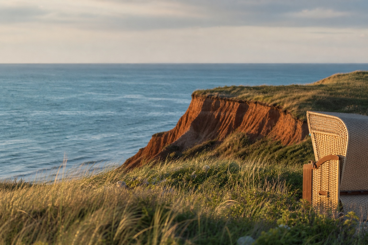 Strandkorb vor roter Kliffküste im Sonnenuntergang auf Sylt. Favorent hilft bei der Verwaltung Ihrer Ferienimmobilie.
