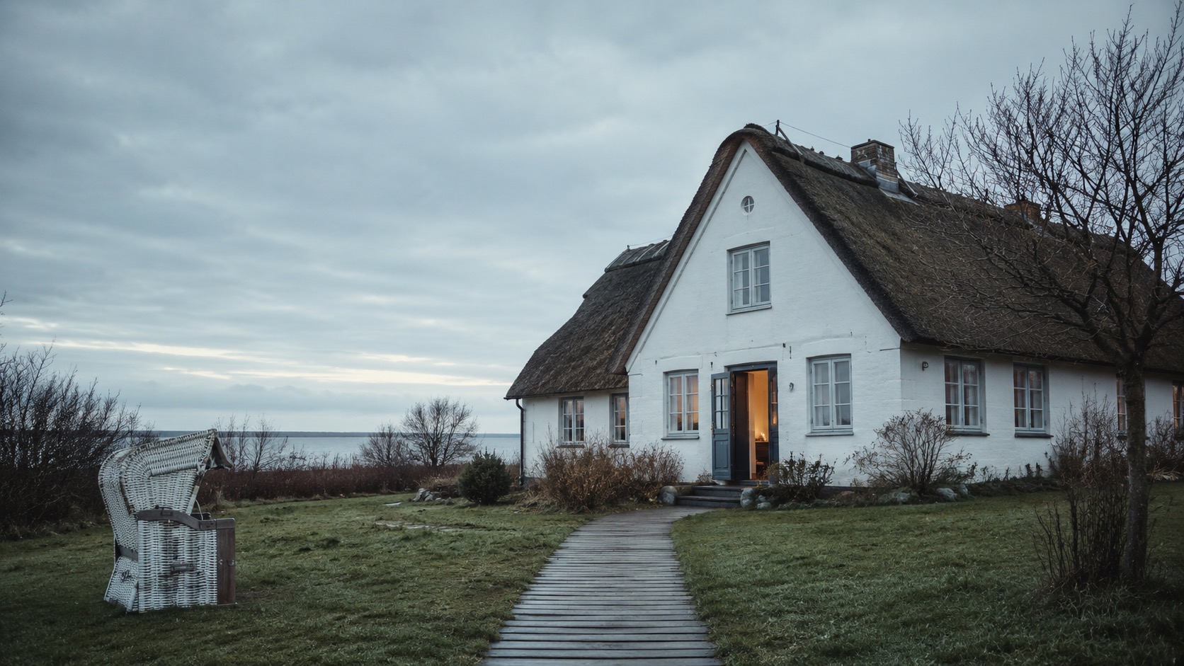 Reetgedecktes, weißes Ferienhaus mit Strandkorb am Meer, verwaltet durch Favorent.