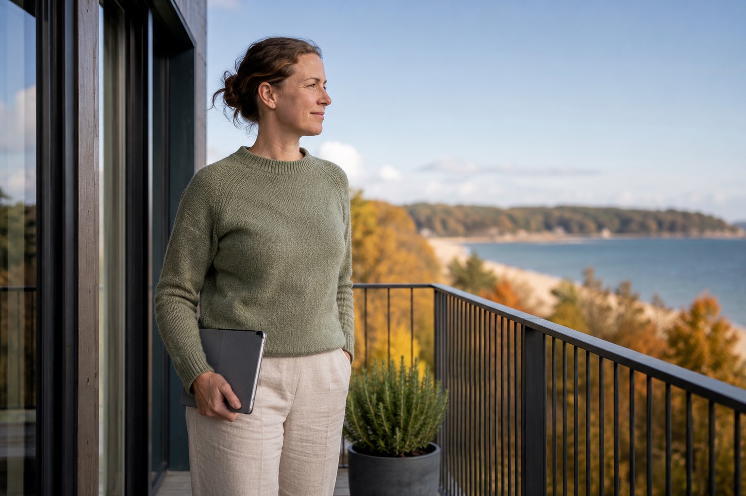 Frau mit Tablet auf Balkon mit Meerblick, während Favorent Ferienwohnungen verwaltet.