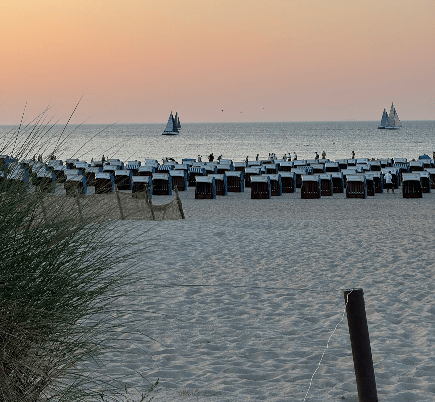 Strandkörbe am Strand von Warnemünde, Segelboote im Hintergrund. Ideal für die Vermietung von Ferienunterkünften mit Favorent.